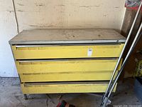 Front view of metal cabinet with three yellow drawers, showing size and condition, with some dirt and rust visible.