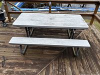 Picnic table showing top and one bench with plastic surface and tubular metal frame on wooden deck