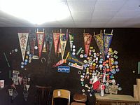 Wall display showing multiple large felt pennants and clusters of round pin-back buttons on dark cork board background.