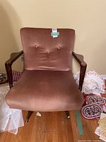 Front view of the dusty rose upholstered swivel rocking chair with wood armrests and button tufted backrest.