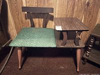 Full front view of wooden telephone table with green vinyl seat showing overall item, legs, and backrest.