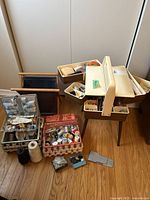 Photo showing plastic sewing kit with swivel drawers filled with sewing notions, two wicker sewing baskets with spools of thread and other accessories, and a cloth knitting bag on the floor.