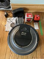 Shark Ion Robot Vacuum RV750 robot vacuum with charging dock, power adapter, extra filter in box, manual and mini handheld vacuum on wooden floor.