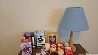 Overview photo of sports bobbleheads in boxes, loose bobblehead, multiple baseballs (some autographed and boxed) and small table lamp with blue shade and wooden base.