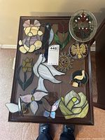 Full assortment of stained glass decor pieces displayed on a wooden table: various floral designs, butterflies, birds, and a sun face.