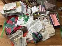 Wide view showing multiple stacks of placemats, napkins, tablecloths, cloth coasters, and wooden napkin rings on a table.