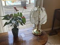 Overall view showing the touch lamp with glass-paneled shades and the faux plant with red and green leaves on a wooden surface near a window.