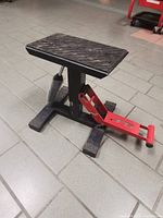 Side view of motorcycle hydraulic lifting stand showing pedal lever and textured platform surface.