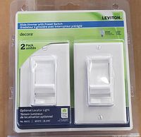 Photo of front package showing two white Leviton Decora slide dimmers with preset switches in sealed plastic packaging with product details and branding.