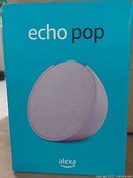 Front of box showing Amazon Echo Pop smart speaker image and branding in lavender color.