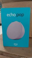 Front of turquoise blue box showing Amazon Echo Pop smart speaker front image and branding.