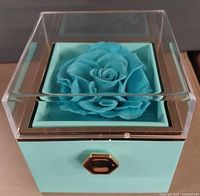 Box top with clear acrylic cover displaying preserved blue rose inside a turquoise and gold box.