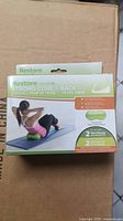 Box front showing the Restore Strong Core & Back Kit branding, a woman using one of the green therapy balls during an exercise on a mat.