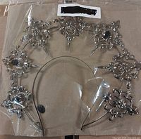 Metal gothic headband with ornate floral and spike designs, missing some black jewel embellishments, sealed in plastic packaging.
