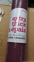 Photo showing the rolled yoga mat with packaging label indicating 'extra thick' and reversible properties, brand Jogi.
