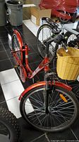 Red Paris Electric bicycle showing frame, thin tires, black front fender, front basket and rear wheel with rack.