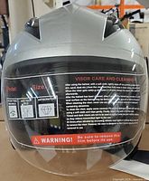 Front view of silver motorcycle helmet showing visor with care and cleaning instructions, size label and anti-scratch, anti-fog features.