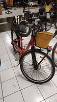 Full view of the red Milan electric bicycle with front wicker basket and rear rack, showing frame and tires.
