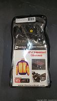 Front view of Venture Heat 12V Heated Gloves in original sealed packaging. Shows branding, product name, size XL, and heating element illustration.