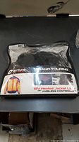 Front of sealed packaging showing Venture Heat Grand Touring 12V Heated Jacket Liner in black, sealed in plastic pouch.