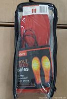 Clear front view of sealed Venture Heat heated insoles in packaging, showing red insoles and wiring inside a transparent plastic case.