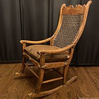 Antique wooden rocking chair with brown vinyl cushion on seat, showing handwoven cane backrest and wooden frame.
