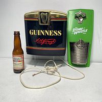 Front view of Guinness bar light, Steam Whistle bottle opener, and Budweiser bottle showing all three items together with power cord on surface.