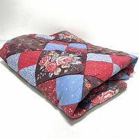 Folded view of the quilt showing the patchwork design with various floral and solid colored fabric squares in red, blue, and brown hues.