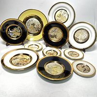 Full set of 12 Japanese Chokin peacock gold plates, showing varied base colors and intricate gilded peacock and floral designs.