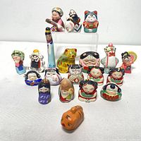 Various angles of 18 hand painted Japanese and Korean clay figures arranged in a group on a white surface.