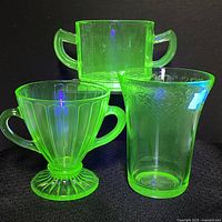 Three green uranium glass pieces brightly glowing under UV light on black background
