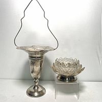 Pair of silver plated floral centerpieces placed side by side; the large pierced motif centerpiece with basket handle and the smaller lotus style flower frog on a stand.