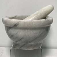 Solid marble mortar bowl with pestle resting inside, showing shape and size of the bowl and natural marble veining.