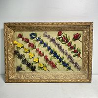 Full view of the Victorian shadow box showing the gold ornate frame and multicolored wire flower garlands arranged diagonally on fabric.