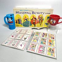 Full lot with 1958 Sleeping Beauty game box, blue Mickey cup, red Mickey and Minnie mug, Minnie n Me collector cards laid out, and Mickey watch on display.
