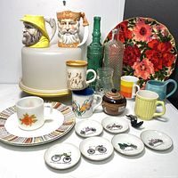 Front view of vintage kitchen lot showing character mugs, plates, mugs, bottles, and decorative dishes