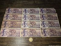 Twelve 100 peso Mexican paper banknotes arranged in a 3x4 grid on a wooden surface with one 10 peso coin placed in front.