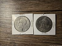 Obverse and reverse sides of the two Eisenhower Liberty Bell silver dollars, each in a white paper coin holder, showing the Liberty Bell on the reverse and Eisenhower portrait on the obverse with the bicentennial dates 1776-1976.