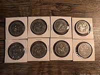 Top side of eight Canadian silver dollar coins in white cardboard holders, showing provincial symbols and designs on reverse sides.