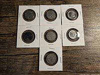 Seven Canadian nickels in white coin holders; five from 1920s-30s showing 'Canada Five Cents' maple leaf reverse, two with rabbit design dated 1997 and 1998.