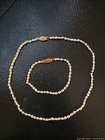 Photo showing a freshwater pearl necklace and matching bracelet with goldtone clasps on a black textured background.