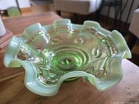 Close-up image of green opalescent glass bowl highlighting ruffled edge and opalescent sheen.
