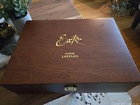 Closed dark wooden presentation box with gold embossed lettering for Lehraud XO Cognac on the lid, shown on wooden floor near furniture and plants.
