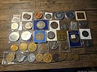 Top angle photo showing the full collection of commemorative coins and medallions laid out on a wooden surface, varying in size and packaging.