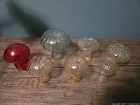 Front view of eight mushroom-shaped colorful ribbed glass propagation vases arranged on wood surface