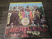Front cover of The Beatles Sgt. Pepper's Lonely Hearts Club Band vinyl album, showing colorful group photo and floral text.