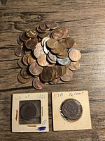Top view of a pile of mixed U.S. pennies and two older coins in cardboard holders with plastic windows. The older coins are labeled 'US 2¢ 1866' and 'USA 1/2 CENT'.