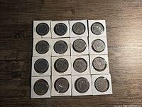 Full view of all 16 Canadian silver dollar coins in individual holders arranged in a 4x4 grid on a wooden surface.