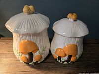 Two ceramic mushroom canisters, larger and smaller, sitting side by side showing overall design and condition