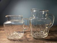 Two clear glass pitchers, one smaller and one larger, with sunburst textured glass pattern showing all angles.